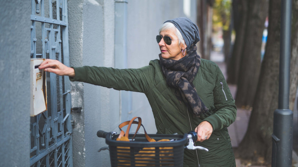 Senior Woman On Bike Getting Letter From Mail Box